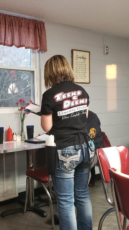 A server in a Teens & Deens shirt by the red-and-chrome diner chairs