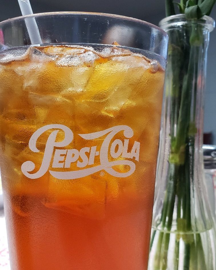 Sweet tea in a Pepsi-Cola glass next to a small vase of flowers